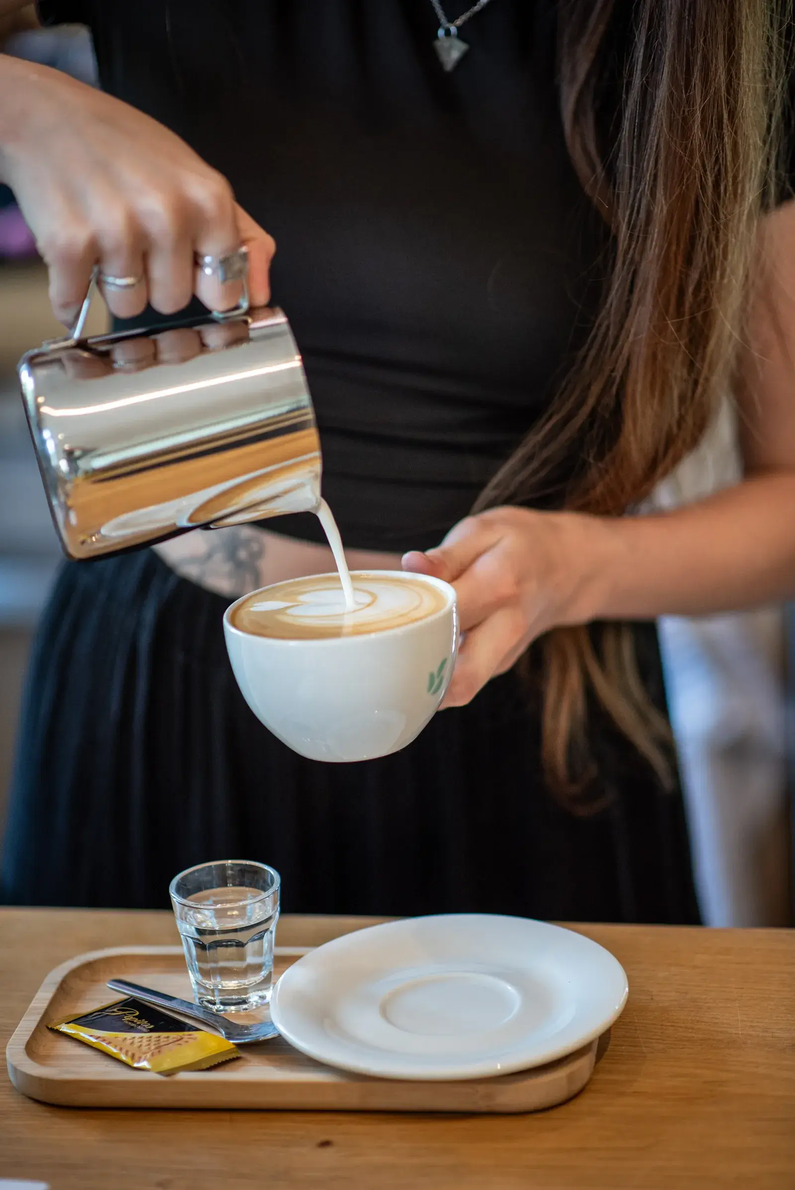 Baristka nalévá mléko do šálku a maluje latte art
